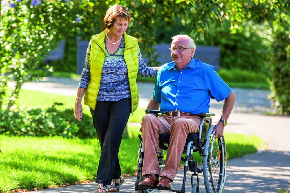Carer walking with man in a wheelchair