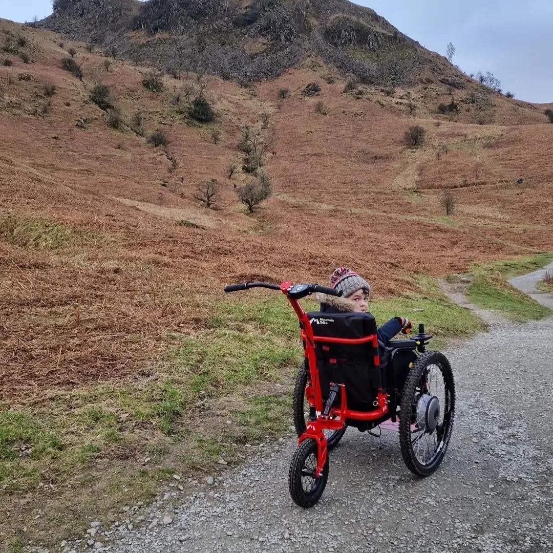 SDMotion Trike All-terrain Powerchair with push handles in front of a hilly path