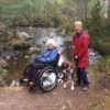 women and wheelchair with dog next to a river