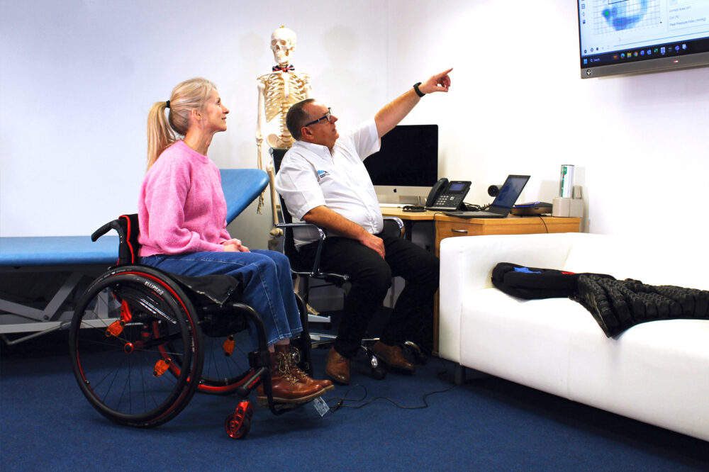 Woman in wheelchair in office looking at wall monitor
