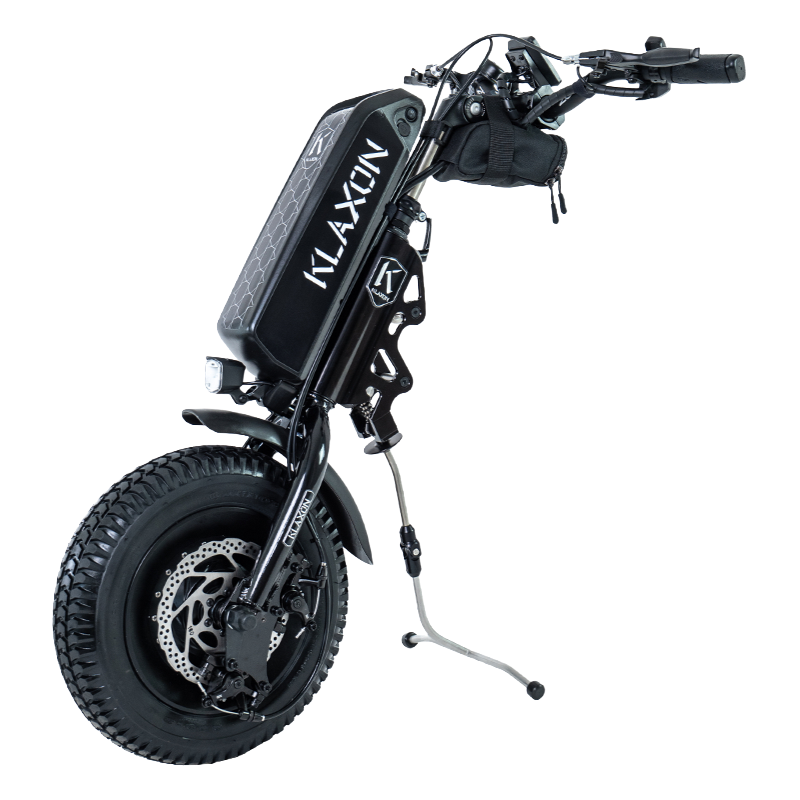 Side profile of the Klaxon Klick Scrambler wheelchair power add-on, featuring a 13.3-inch off-road tire, integrated battery, and the patented Klick linking system for quick attachment to a manual wheelchair, isolated on a white background.