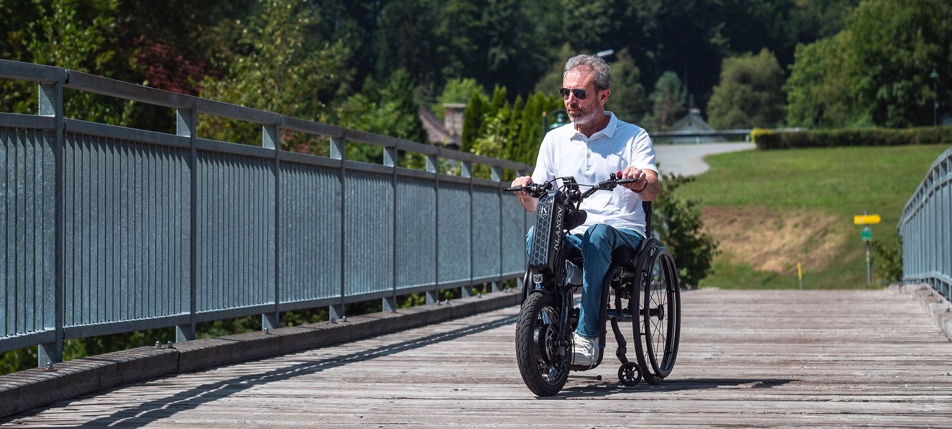 A landscape banner featuring the Klaxon Klick Power Handbike, a high-performance electric power attachment for manual wheelchairs, being used on an outdoor trail.