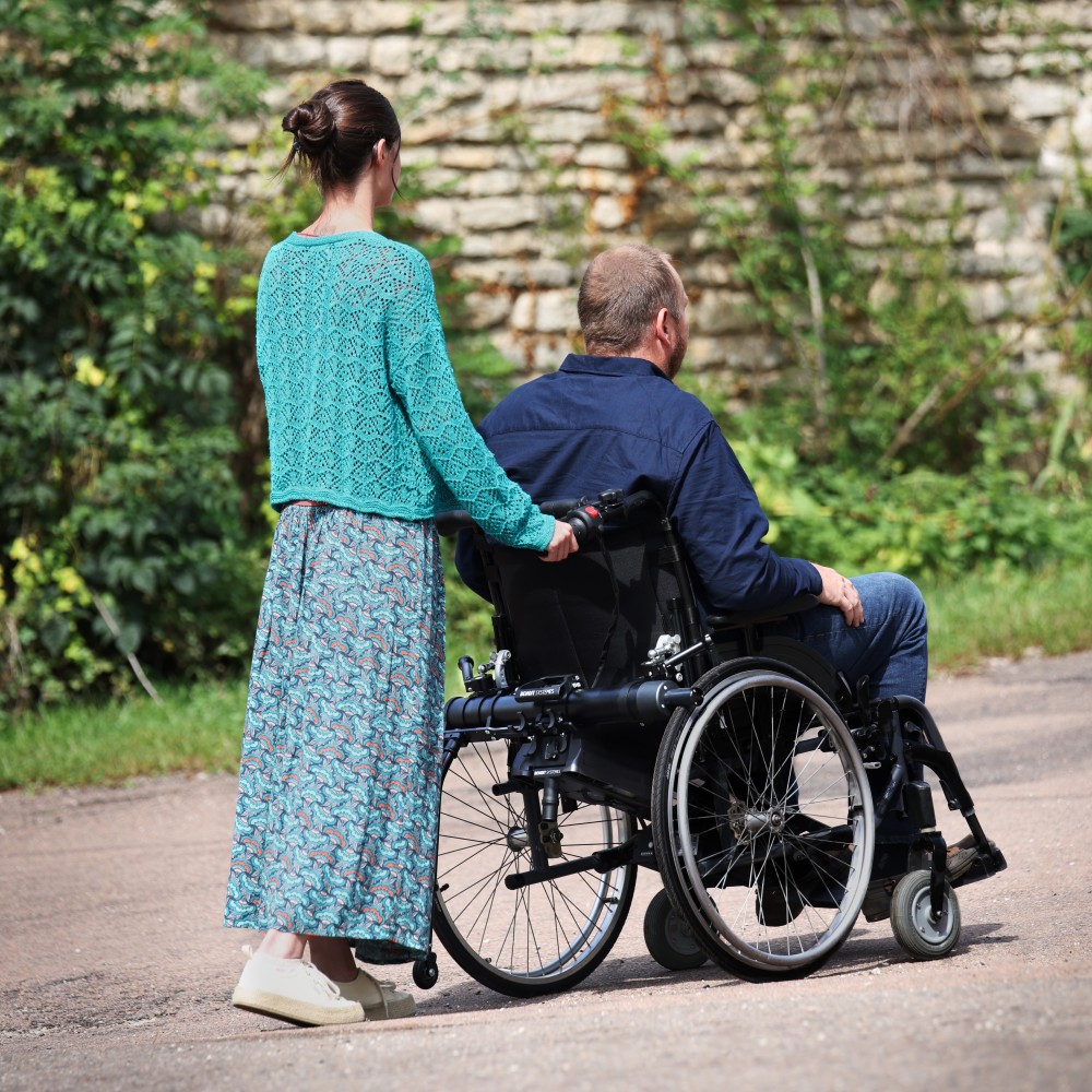 An attendant effortlessly pushing a wheelchair user up a paved incline outdoors, demonstrating the power of the Light Assist 3.
