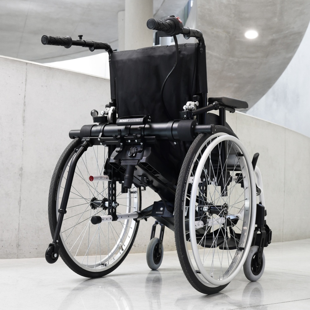 Rear view of the Light Assist 3 power add-on mounted to a manual wheelchair, showcased in a modern, brightly lit indoor setting.