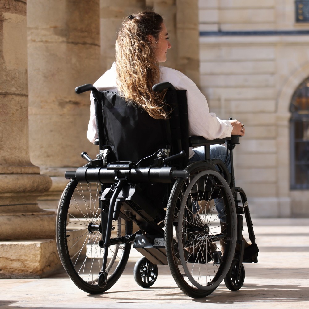 Rear view of the Benoit Systèmes Light Drive 3 wheelchair power add-on unit mounted on a manual wheelchair, showing the motorized drive system and battery.