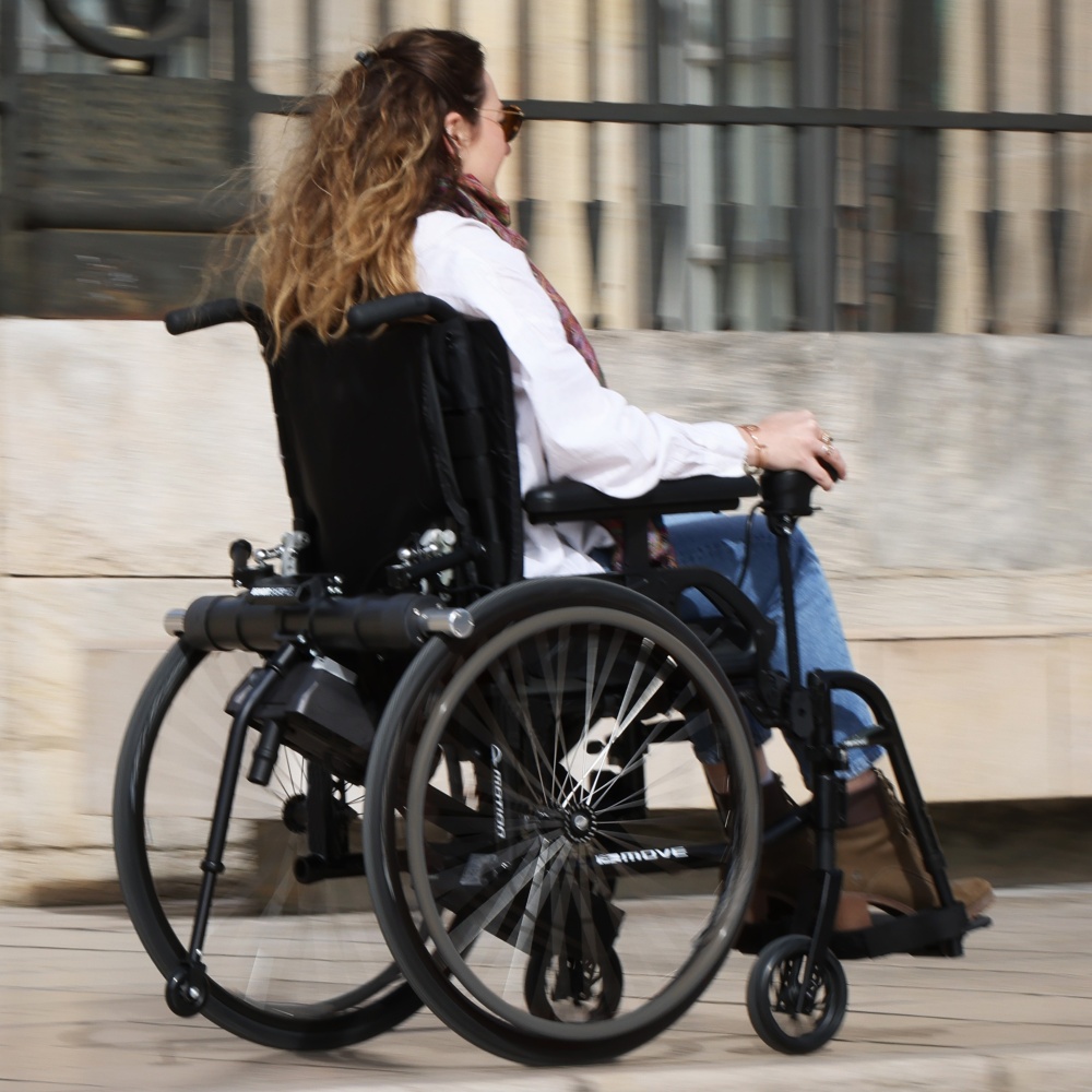 A technical close-up of the Benoit Systèmes Light Drive 3 wheelchair power add-on, showcasing the clutch engagement levers and the motorized drive unit attached to the manual wheelchair.