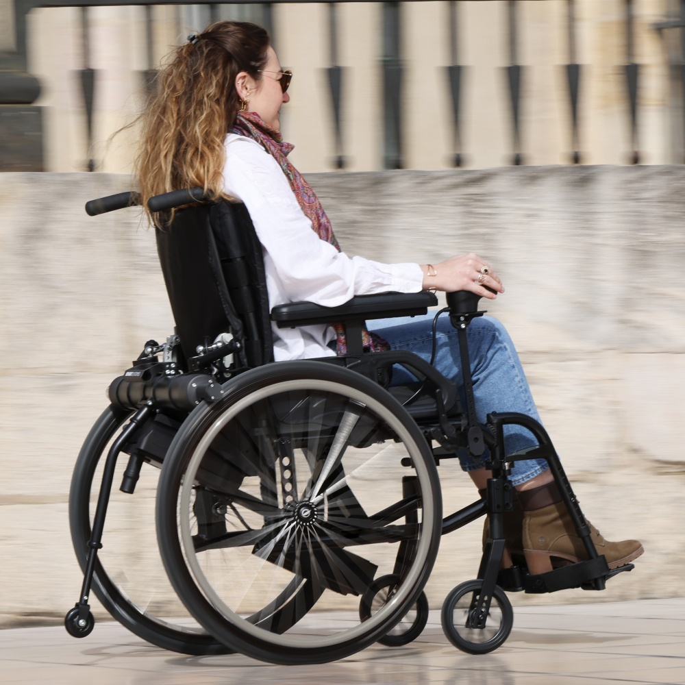 Close-up of the Benoit Systèmes Light Drive 3 wheelchair power add-on, featuring the integrated anti-tip wheels and battery system designed for maximum safety and stability.
