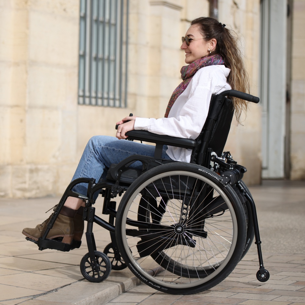 A close-up view of the Benoit Systèmes Light Drive 3 wheelchair power add-on, detailing the connection to the manual wheelchair wheels and the compact drive motor.