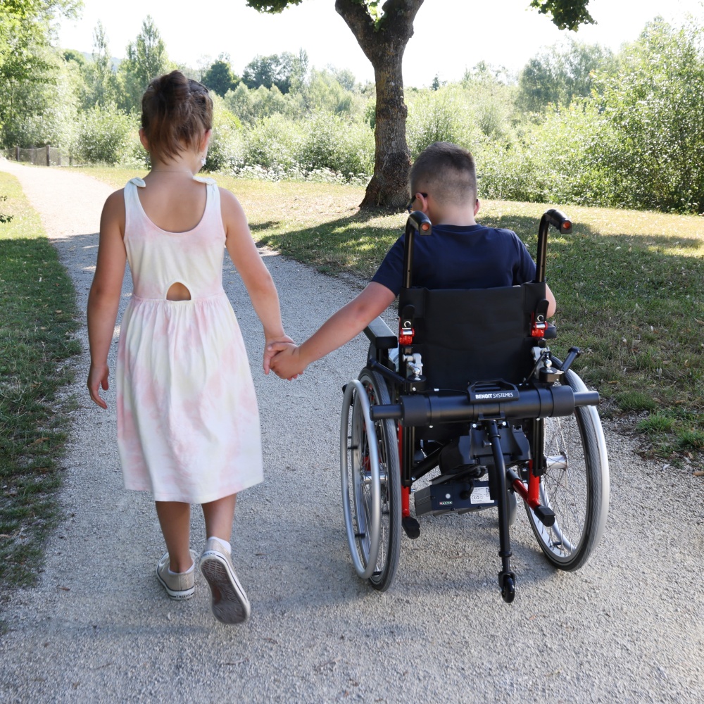 Heartwarming image of a young girl holding hands with a boy in a manual wheelchair equipped with a Light Drive Mini 3.